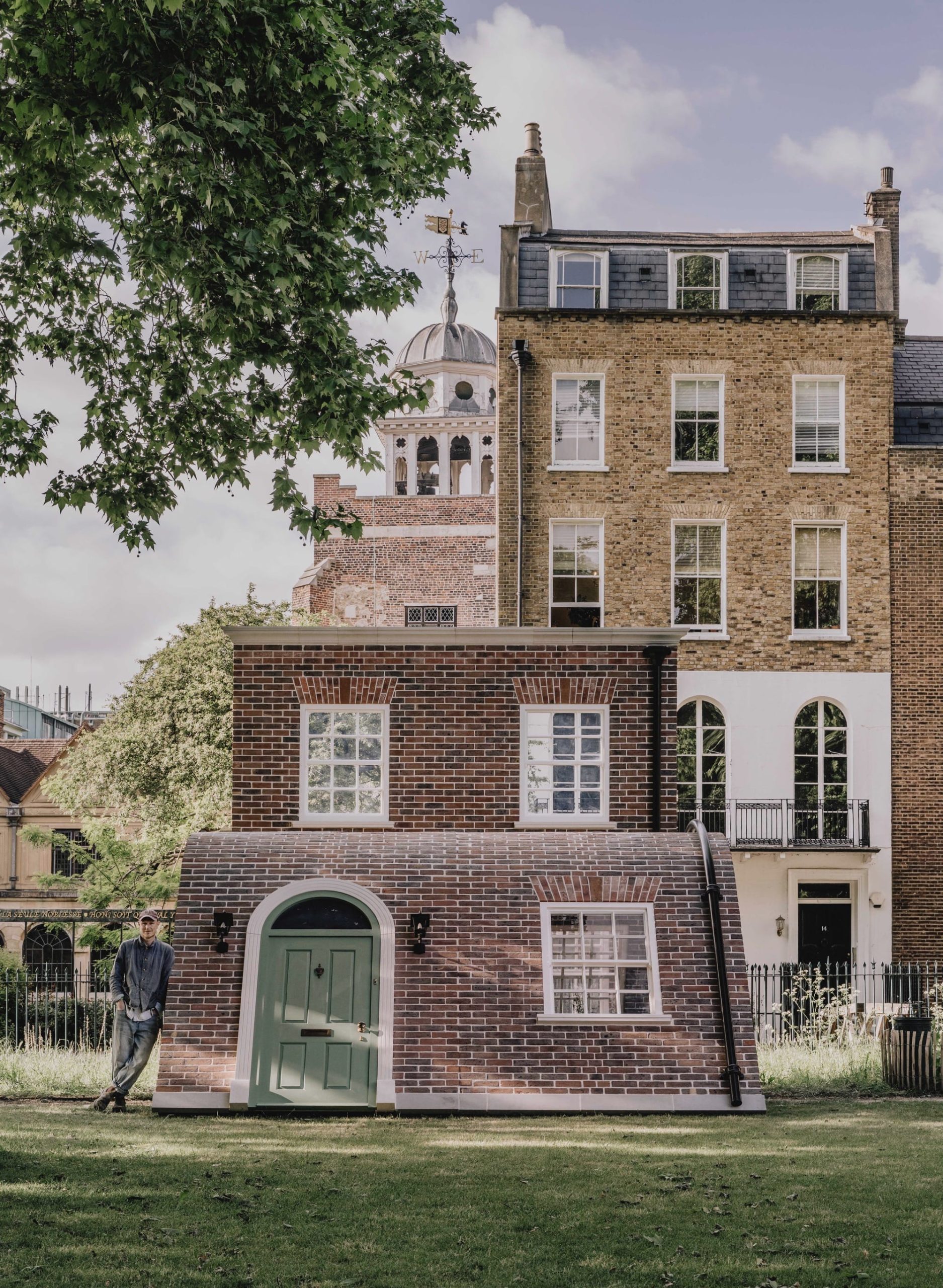 a public art piece in a a park featuring the facade of a London townhouse that appears to sit on the ground with its knees up