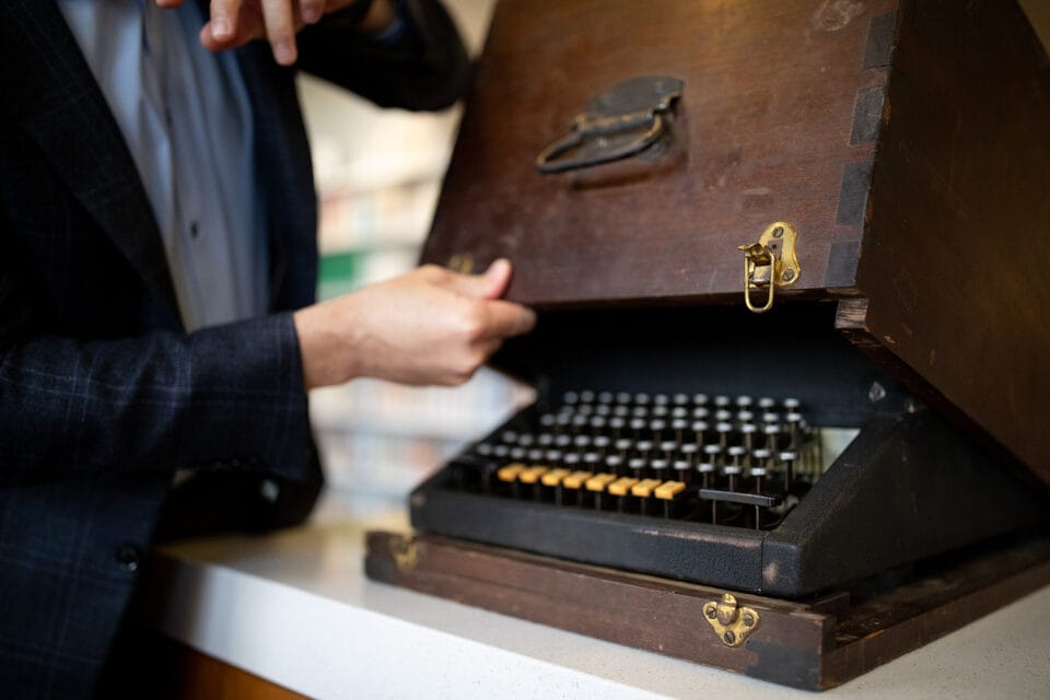 a typewriter is shown as its protective wooden case is lifted off of it