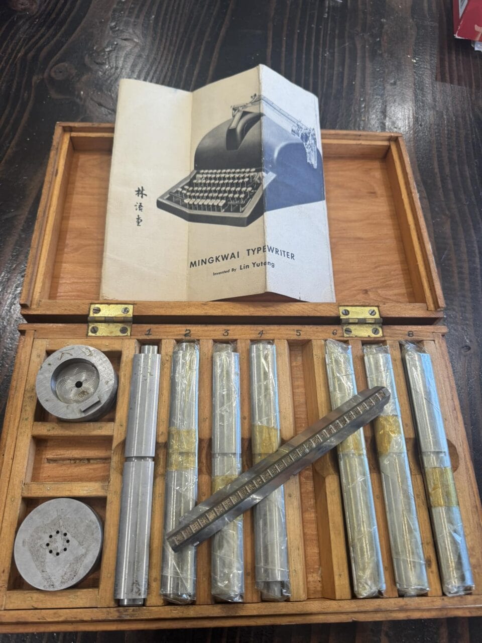a wooden box holds unique Chinese character components for a typewriter, displayed along with a flier